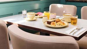 A dining table with a breakfast setting including pastries, a glass of juice, and a cup. - Blandford Hotel (London)