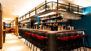 A bar area with a curved counter, multiple shelves stocked with bottles, and red bar stools. - Euston Square Hotel (London)