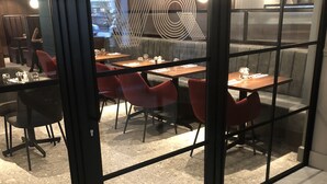 A modern dining area with glass partitions, red chairs, and a central table with a decorative light fixture. - Euston Square Hotel (London)