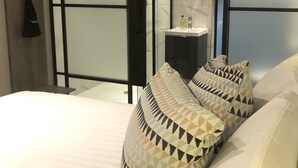 A modern bedroom with a bed, patterned pillows, a bedside table with a bottle, and a hanging garment. - Euston Square Hotel (London)