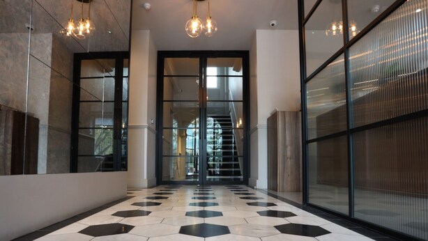 A hallway with a geometric patterned floor, glass doors, and a staircase leading to an upper level. - Euston Square Hotel (London)