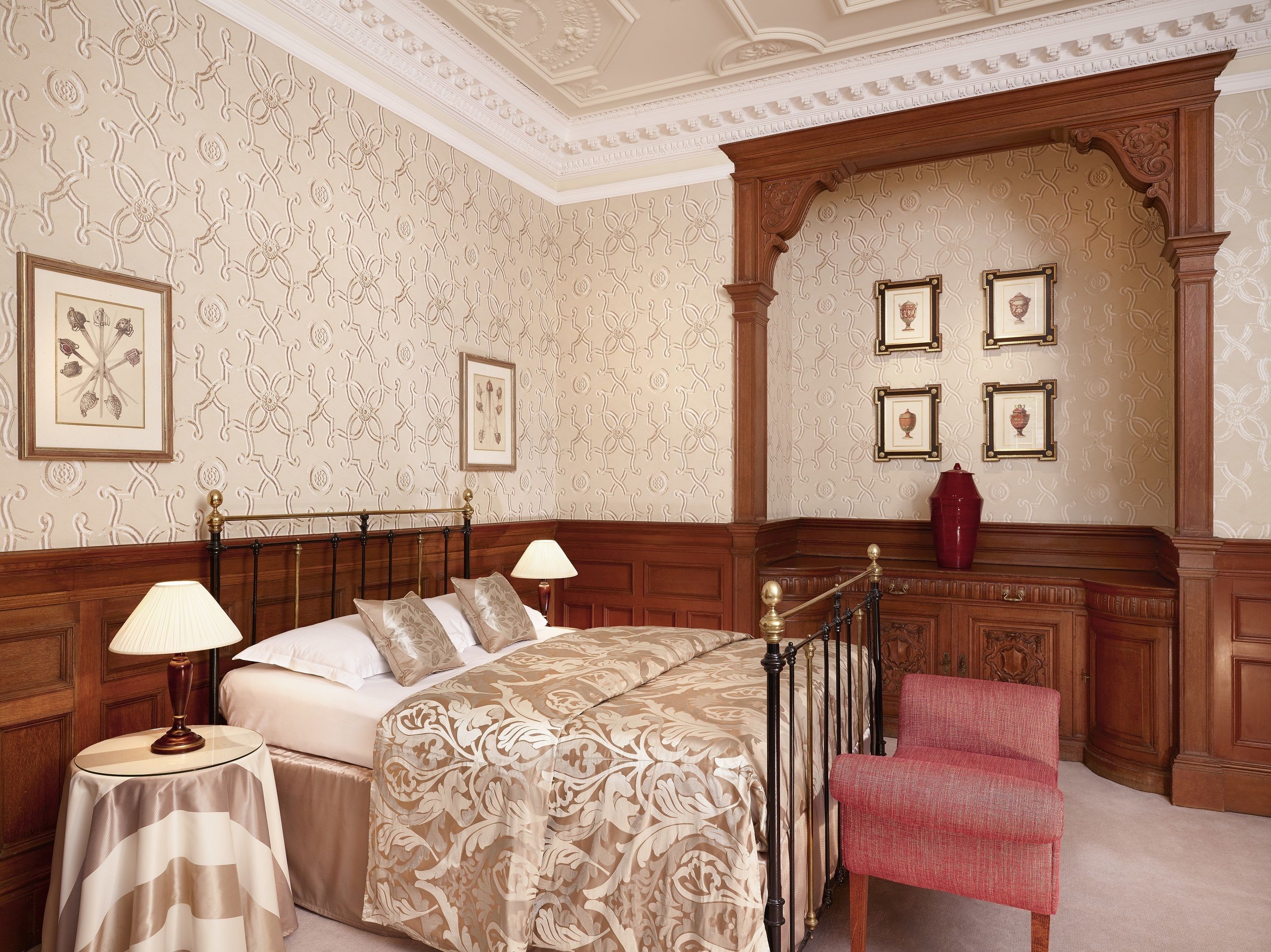 A bedroom with a large bed, two bedside tables, a chair, and a decorative arched niche with framed artwork.