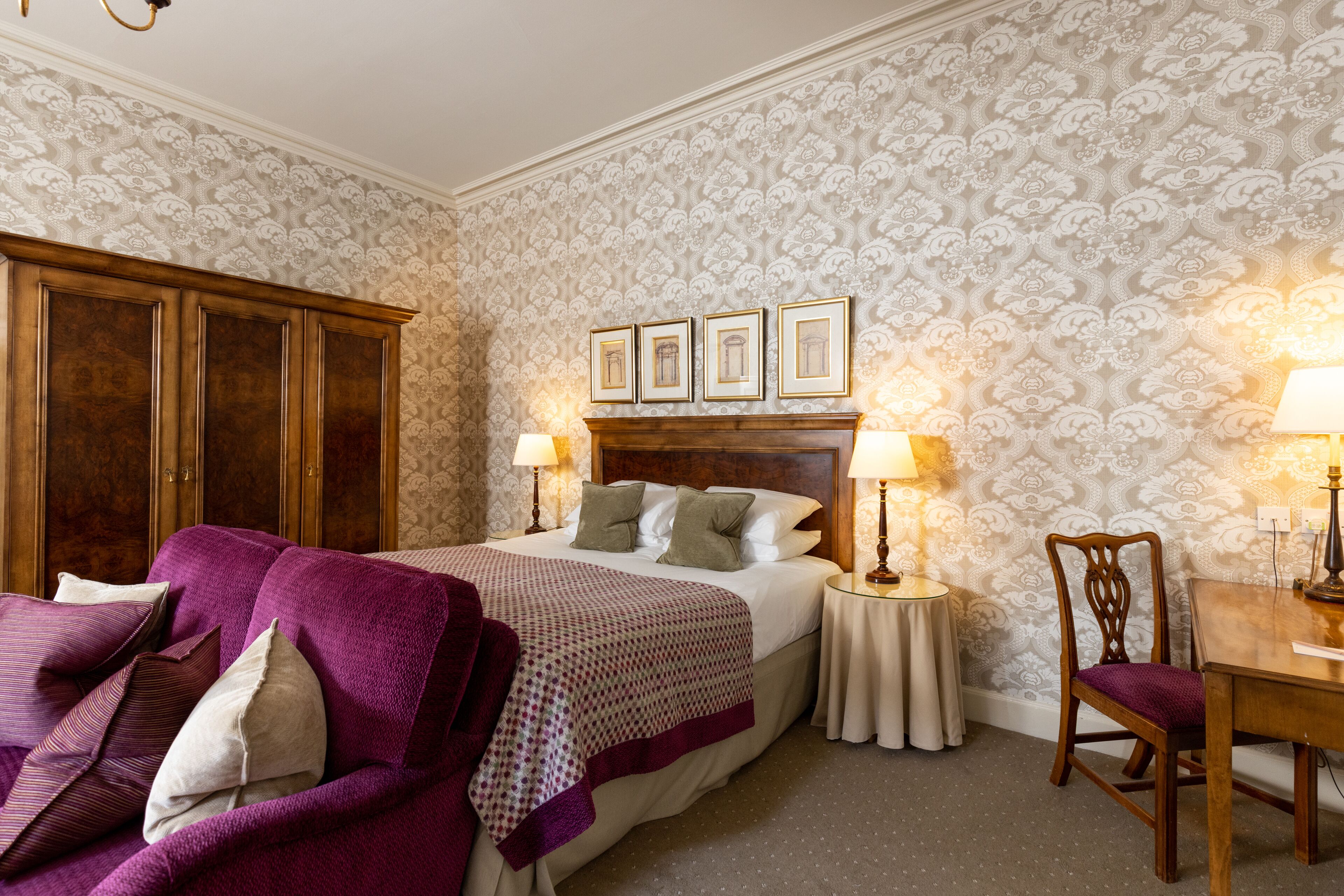 A bedroom with a bed, a wooden wardrobe, a nightstand, a chair, and a table.