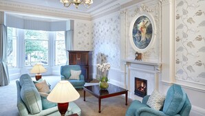 Una sala de estar clásica con chimenea, muebles elegantes y un ventanal con vistas al exterior.
