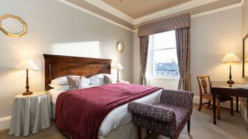 A hotel room with a large bed, two bedside tables with lamps, a chair, a wooden desk, and a window with curtains.