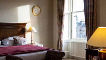 Ein Hotelzimmer mit Bett, Sessel, Lampe, Uhr und einem Fenster mit Vorhängen.