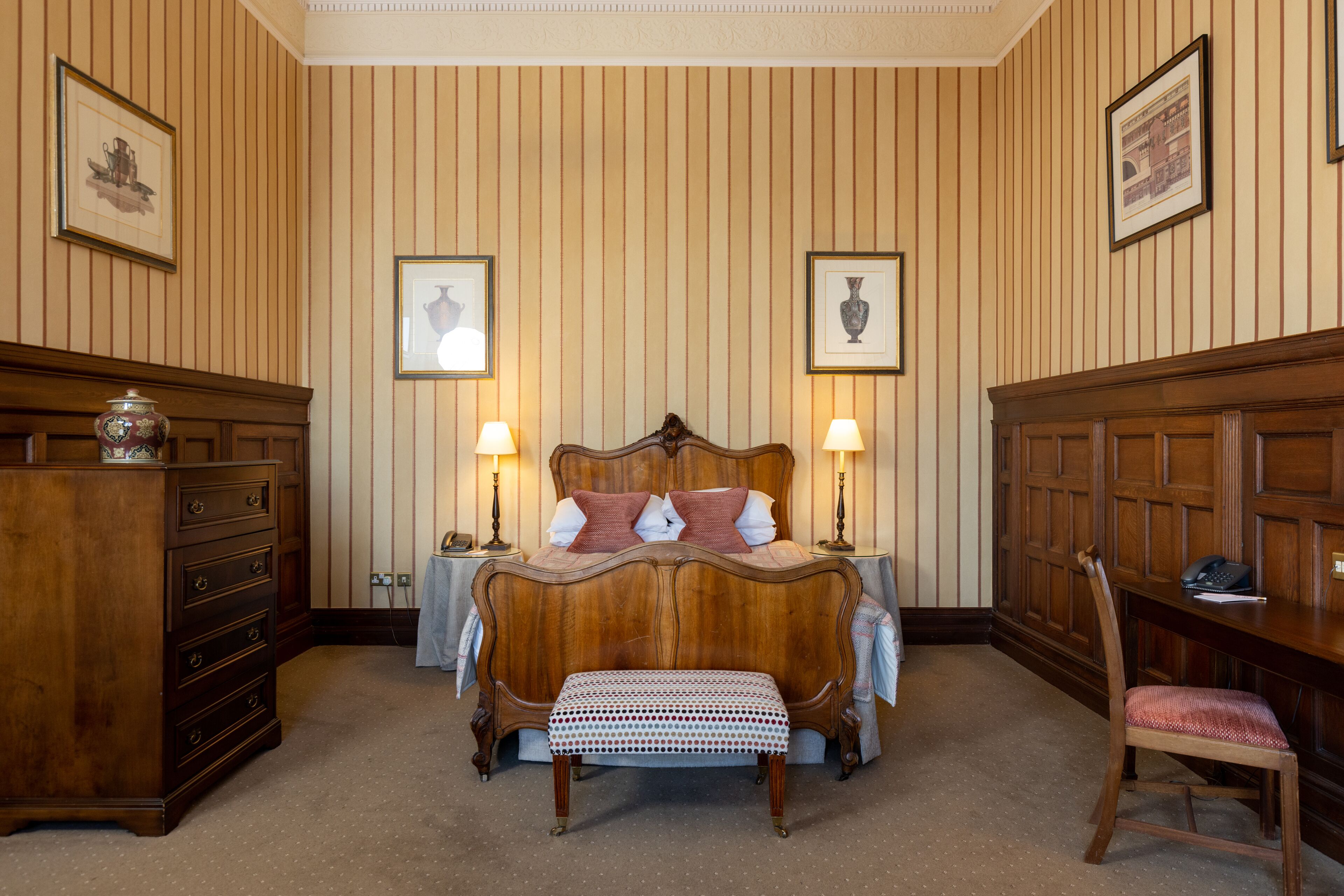 Une chambre à coucher avec un lit en bois, deux tables de chevet avec des lampes, une commode en bois et une chaise.