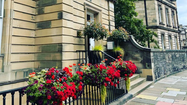 Un edificio histórico con fachada de piedra, una bandera y un parterre de flores.