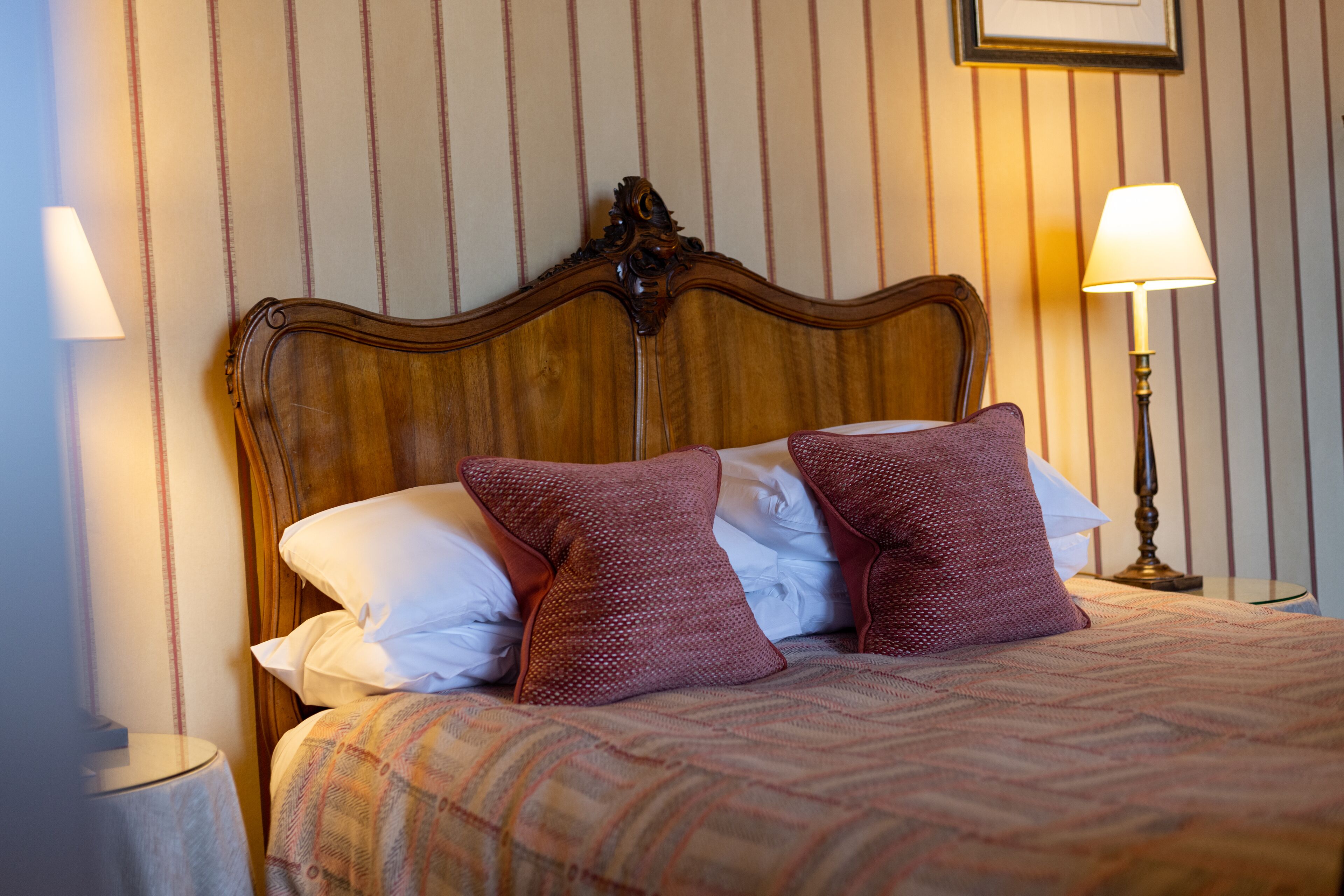 Een net opgemaakt bed met een geborreld sprei en twee decoratieve kussens, een houten hoofdbord en twee bedlampjes op een nachtkastje.