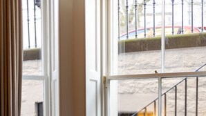 Una habitación con una mesa redonda, dos sillas con cojines morados, una ventana que da a una escalera y un radiador.