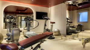 A gym with various exercise equipment, a bench, and a large mirror. - The Memoir Club (London)