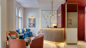 A modern lobby with a reception desk, seating area, and artwork on the walls. - The Memoir Club (London)