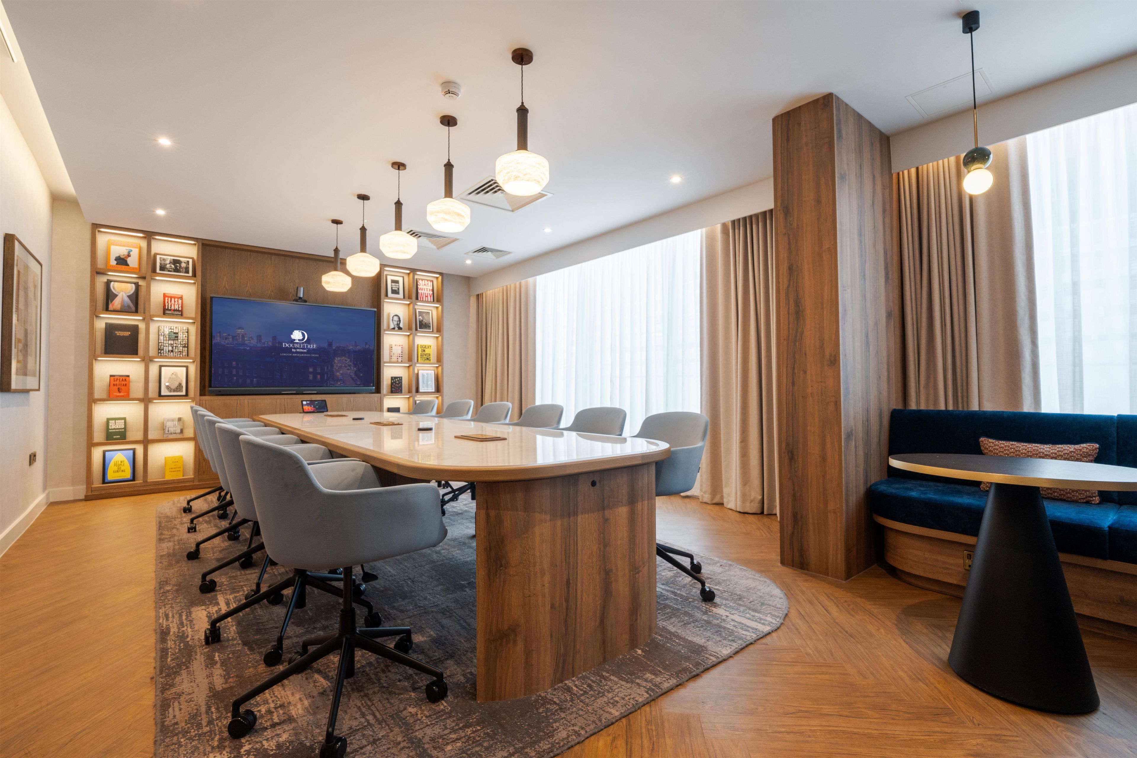 Een moderne hotelkamer met een grote vergadertafel, zitplaatsen, een televisie en een bank.