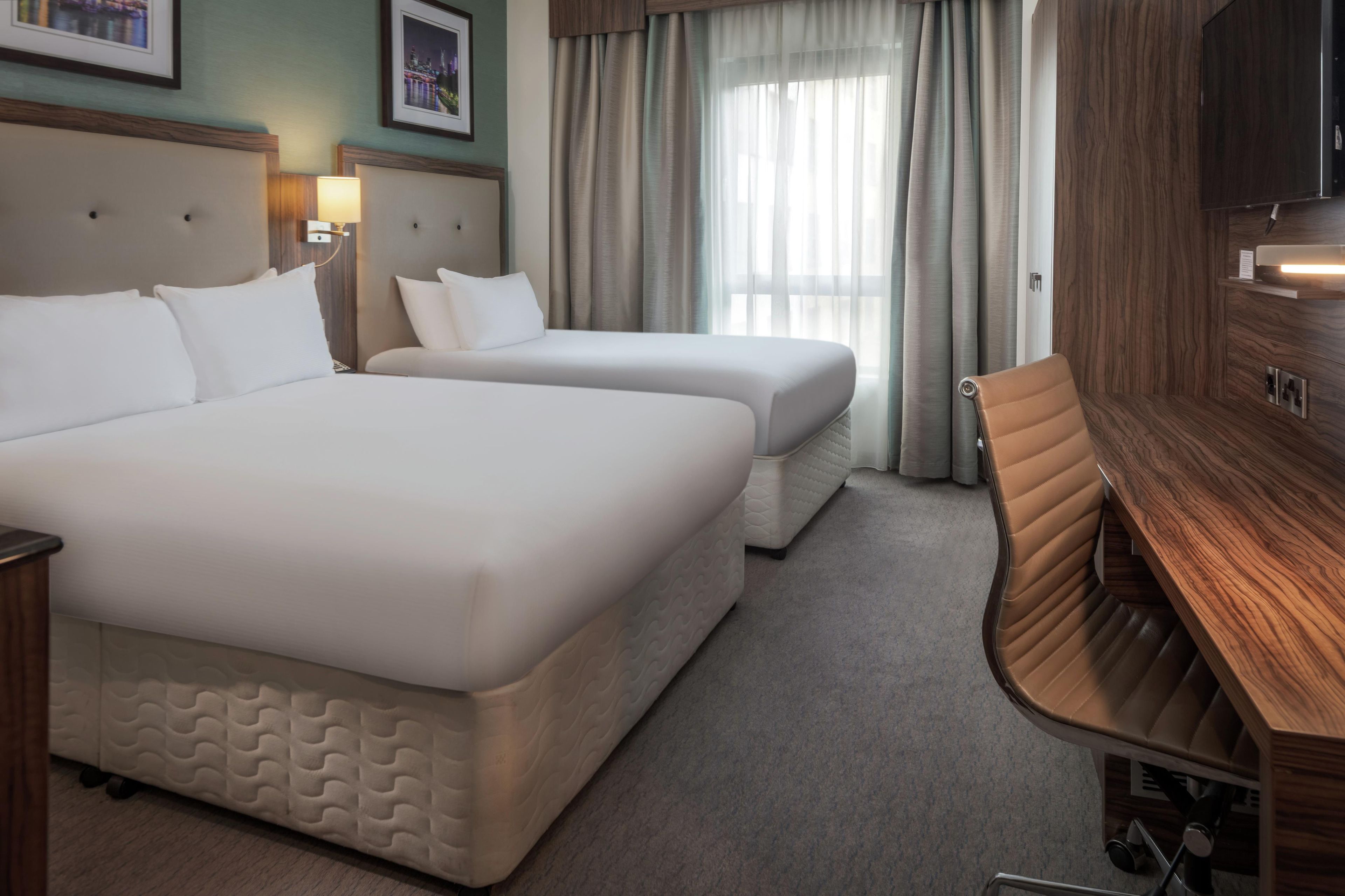 Hotelkamer met twee bedden, een bureau, een stoel, een televisie en een raam met gordijnen.