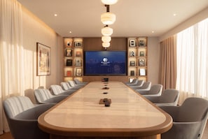 Un salón de conferencias con una larga mesa, varias sillas, un televisor de pantalla plana grande y cuadros en las paredes.