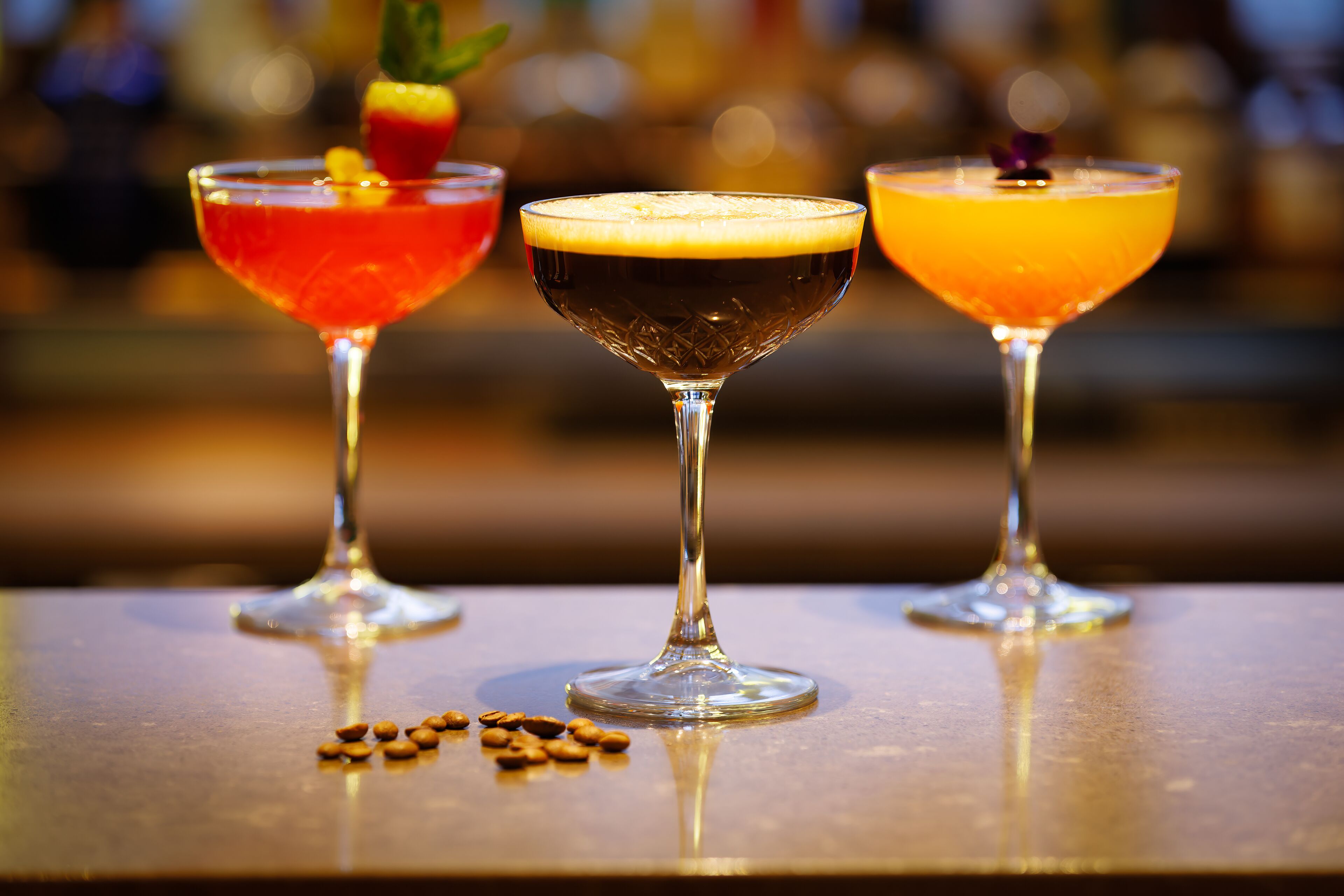 Three cocktails on a bar counter with a blurred background.