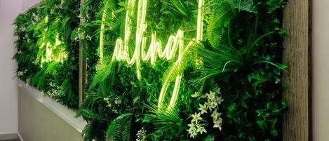 A wall with a neon sign that reads 'talking' amidst lush green foliage.