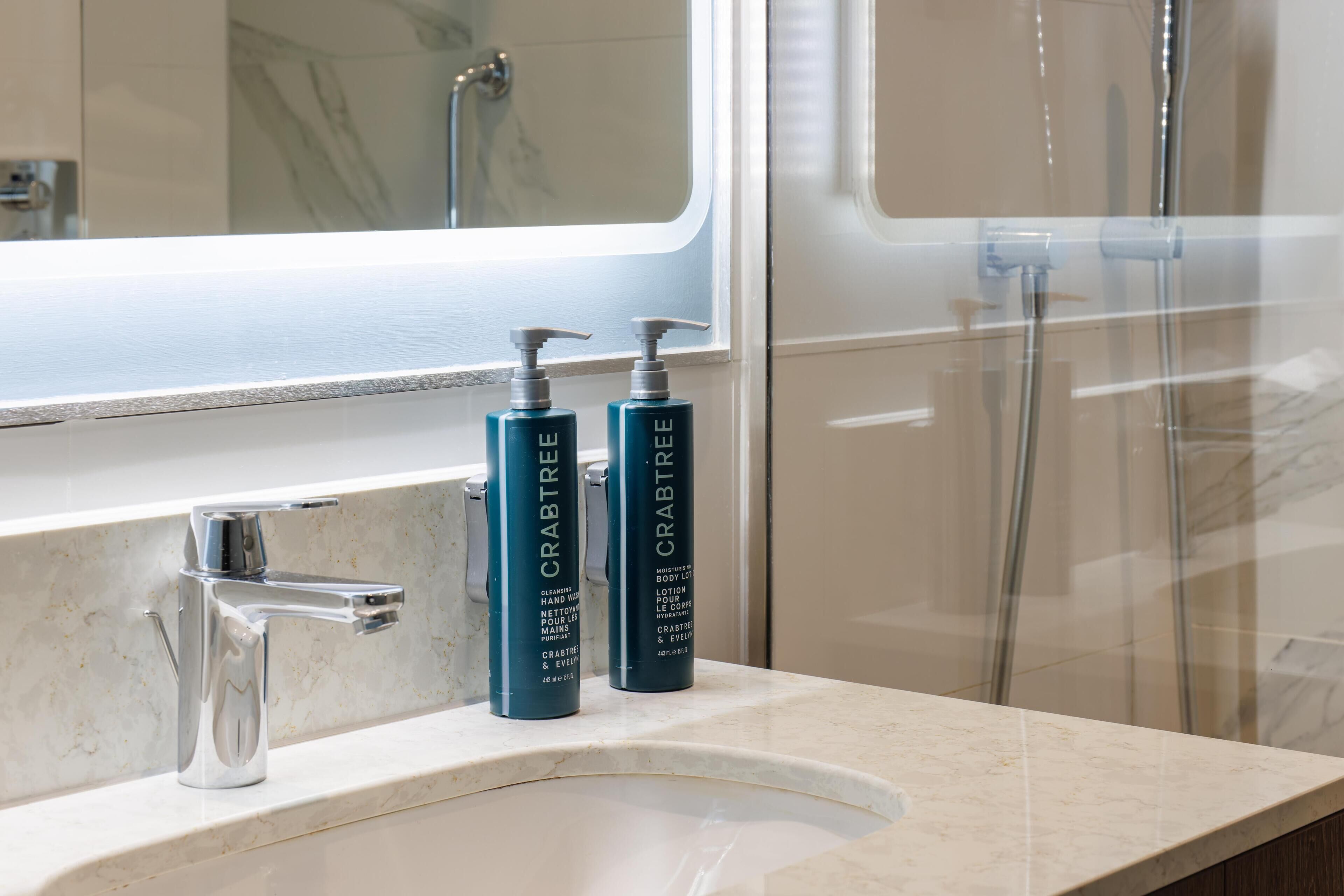 A bathroom with a modern sink, a mirror, and two bottles of Crabtree body wash on the countertop.