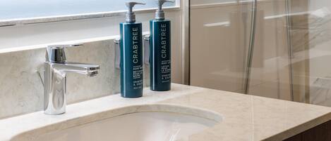 A bathroom with a modern sink, a mirror, and two bottles of Crabtree body wash on the countertop.
