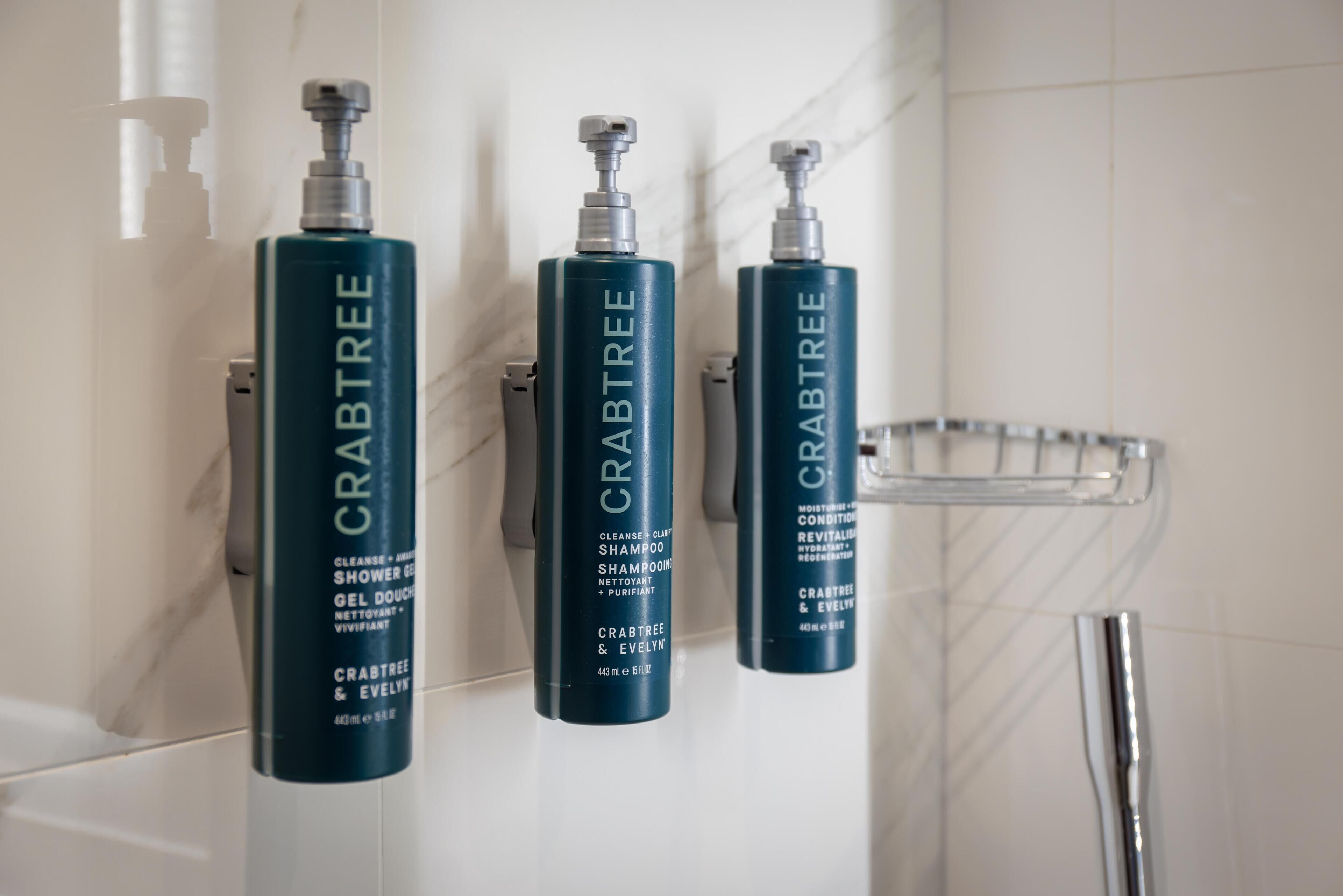 Tres botellas de champú y acondicionador de Crabtree & Evelyn en una pared de baño.