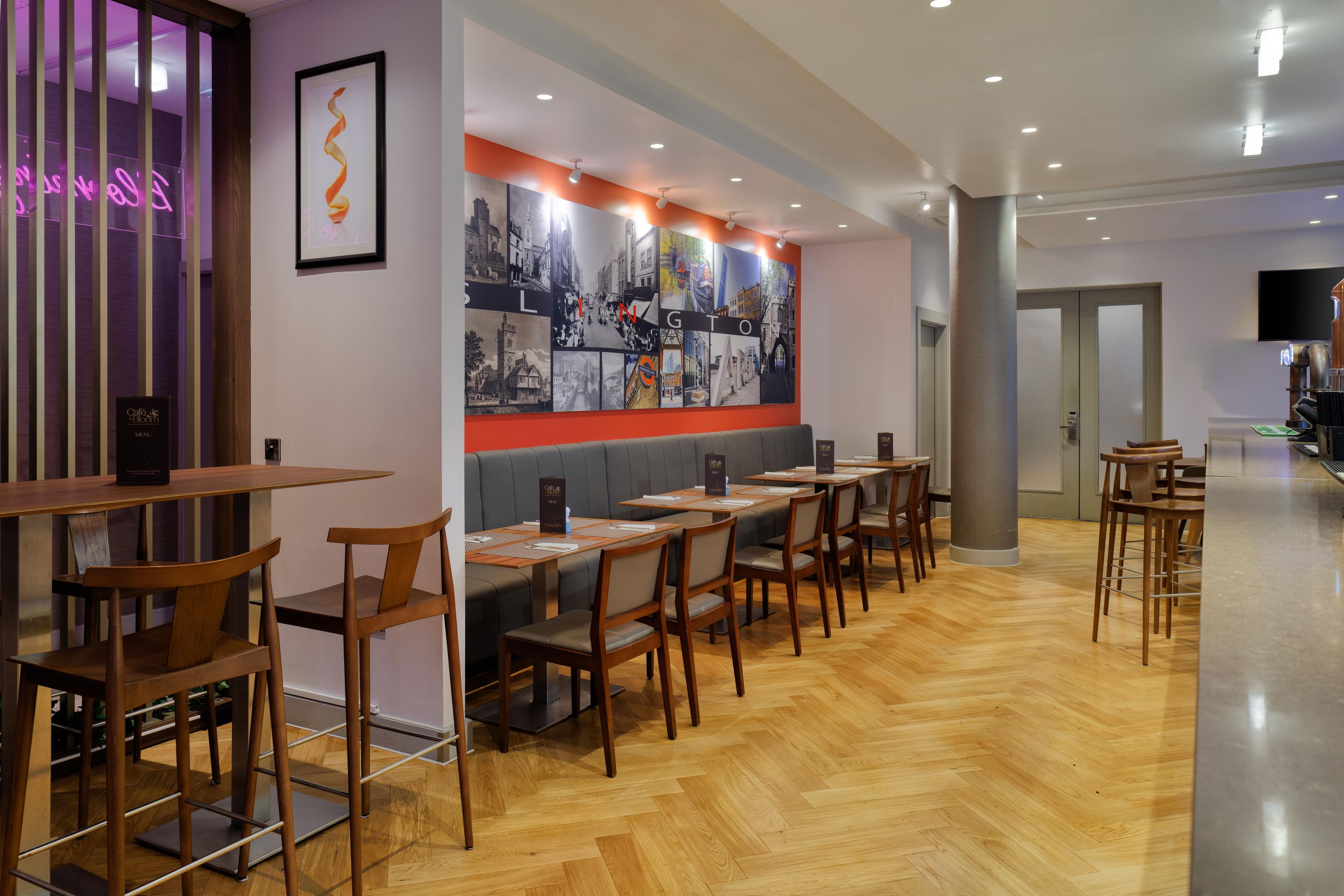 A restaurant with wooden tables and chairs, a menu stand, and a wall with a cityscape mural.