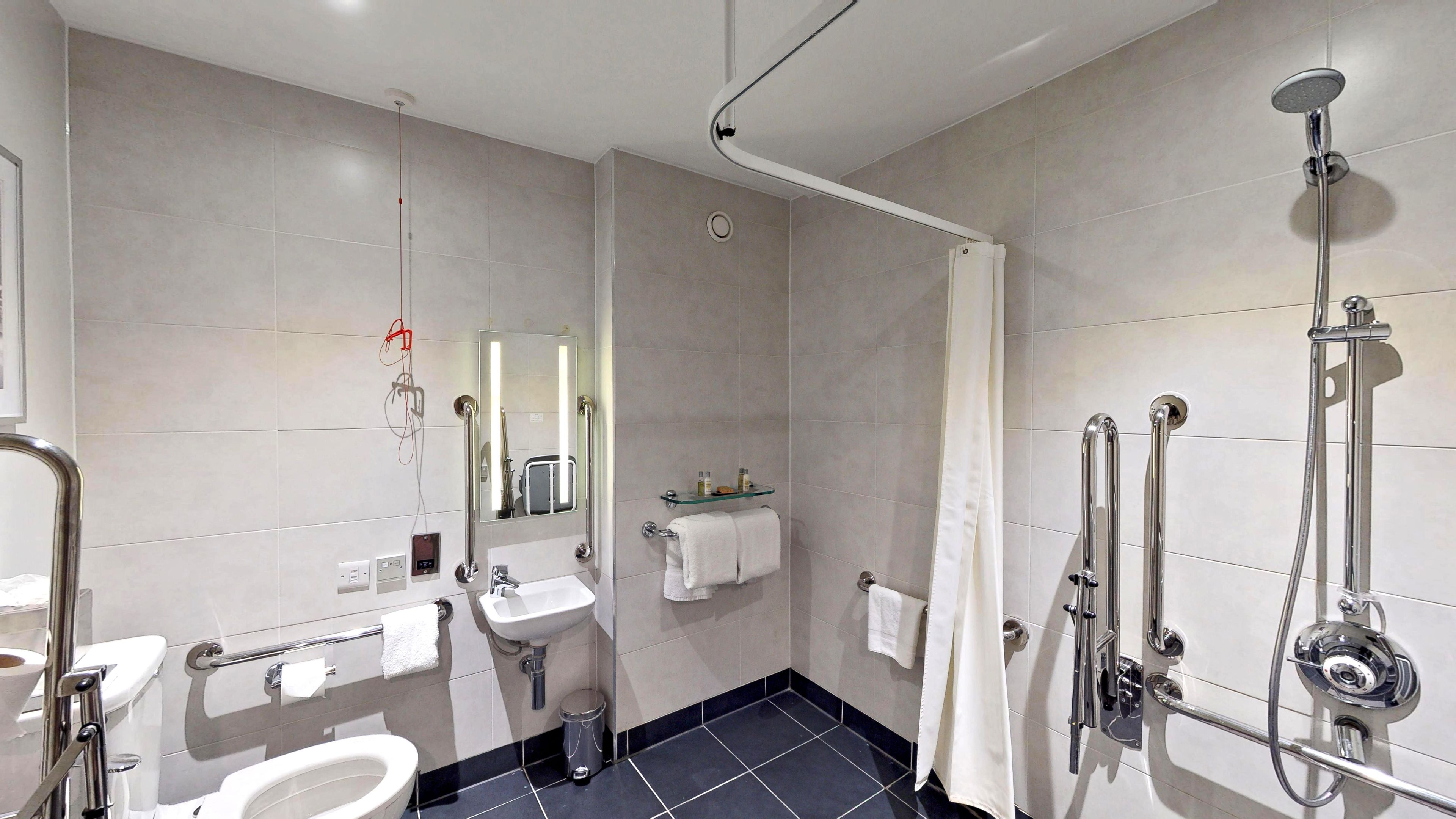 Een moderne badkamer met toilet, wastafel, spiegel en douche met handgrepen.