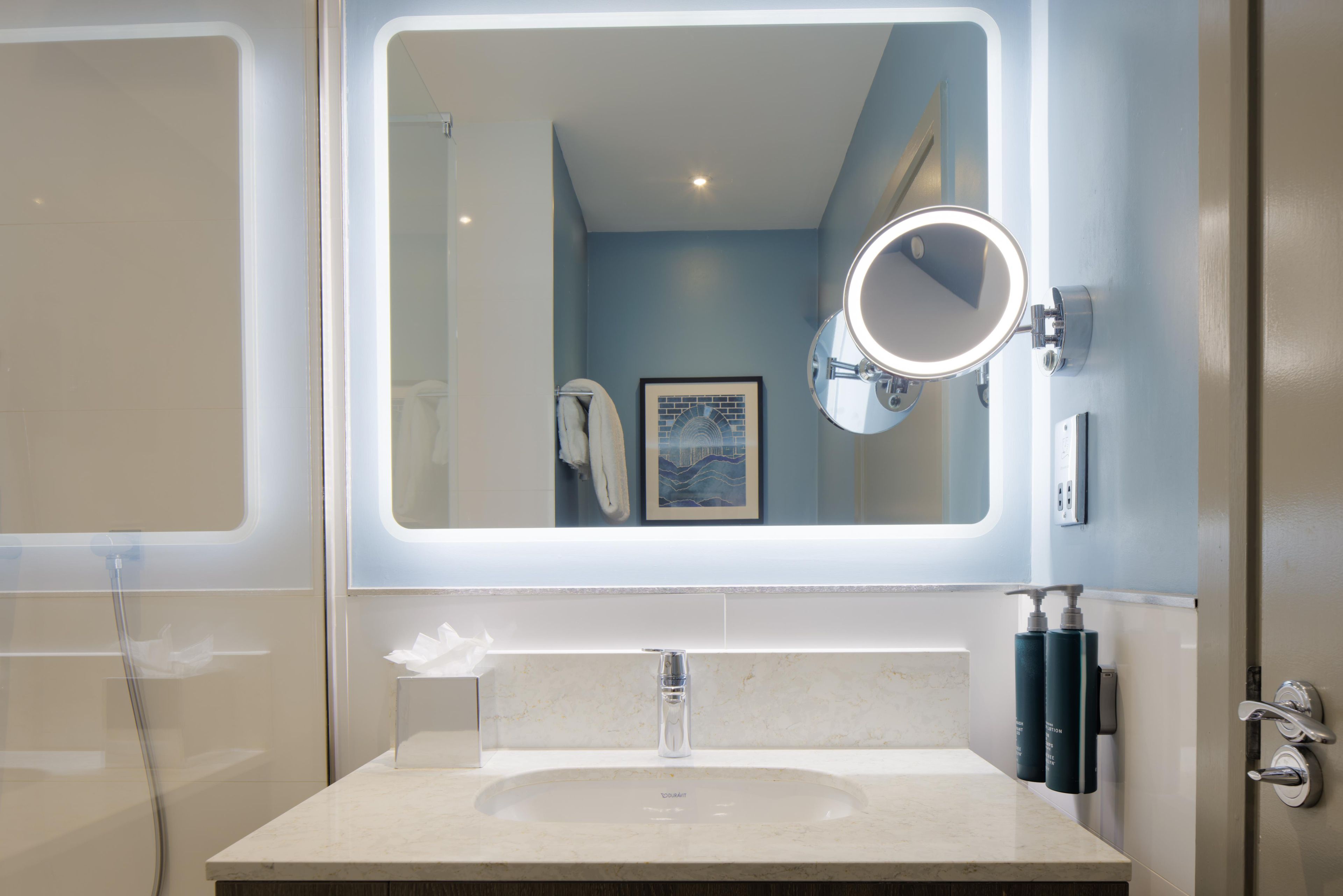 Une salle de bain avec un grand miroir, un lavabo et un porte-serviettes.
