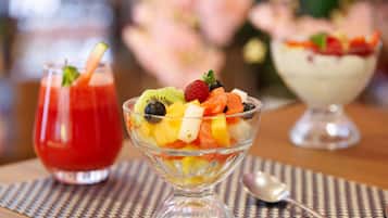 A dessert table with three bowls of fruit and a glass of red drink.