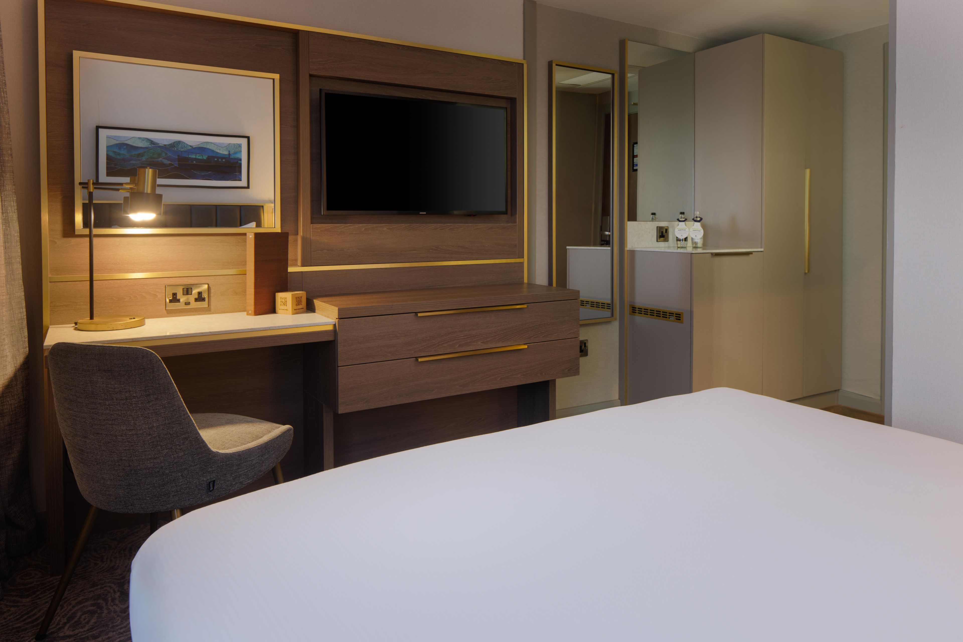 Una habitación de hotel con una cama, un escritorio, una silla, un televisor y un armario.