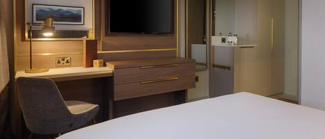 Una habitación de hotel con una cama, un escritorio, una silla, un televisor y un armario.
