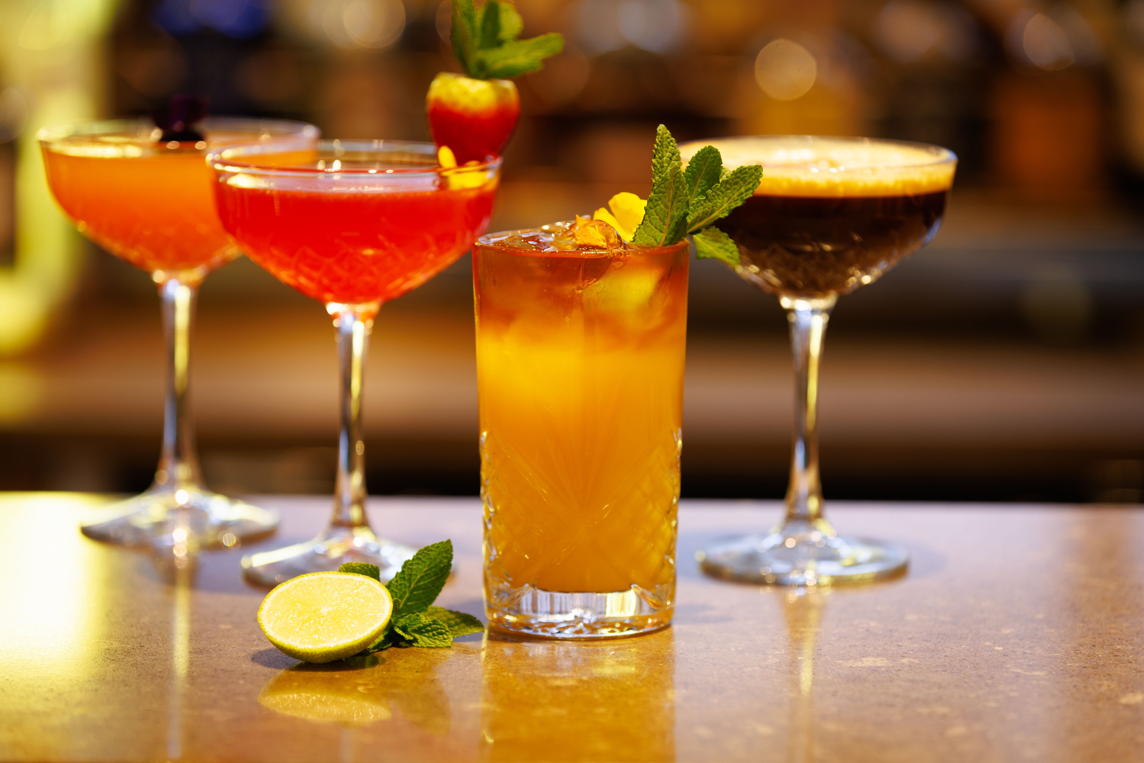 Four cocktails on a bar counter with a blurred background.