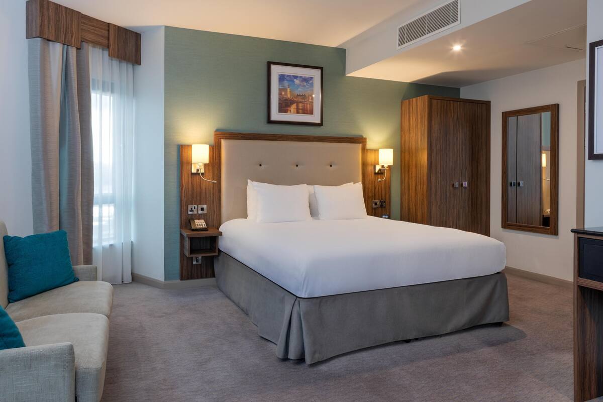 A hotel room with a bed, a nightstand, a chair, a wardrobe, and a framed picture on the wall.