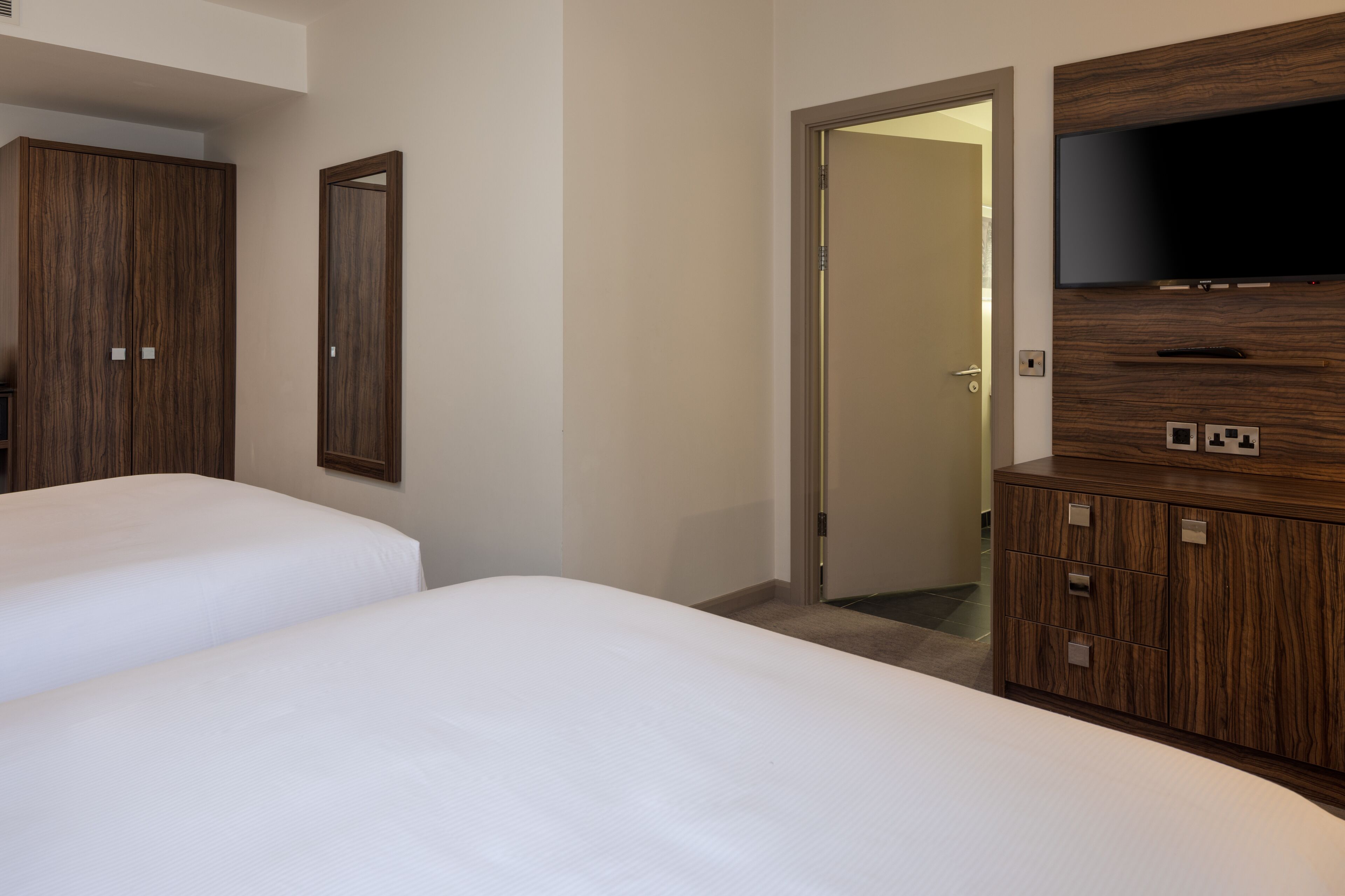 Une chambre d’hôtel avec deux lits, une armoire en bois, une télévision et une porte donnant sur une autre pièce.
