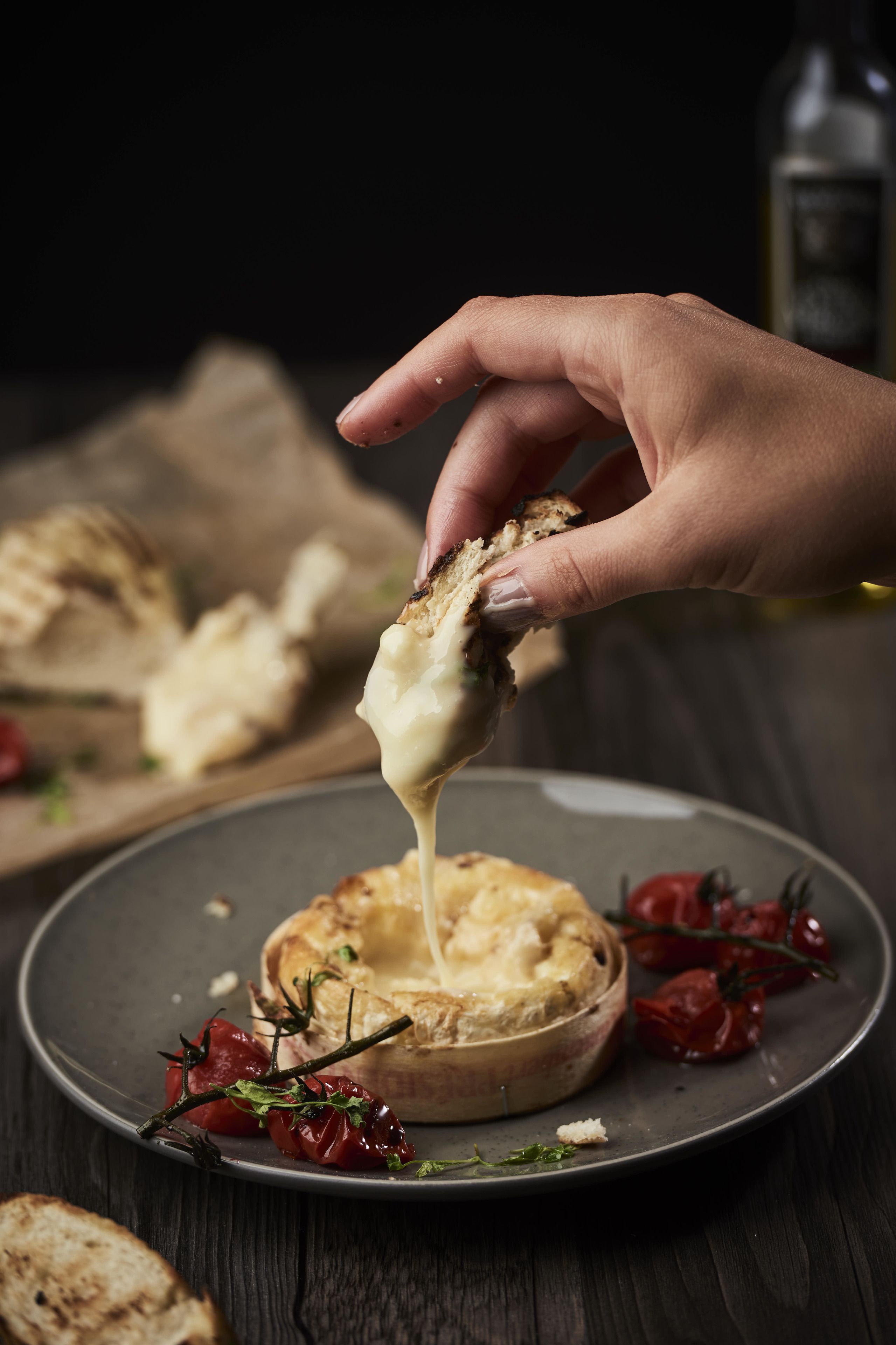 Une main tenant un morceau de pain recouvert de fromage fondu.