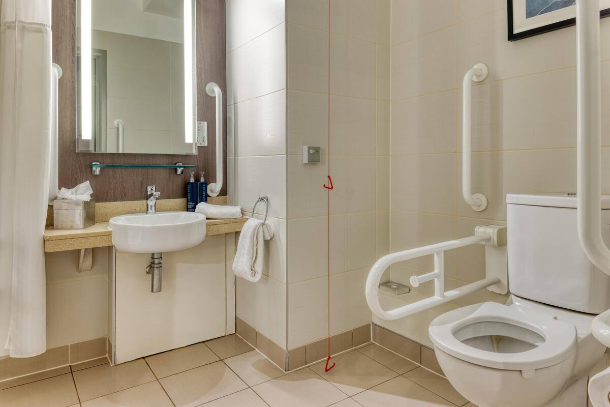 A modern bathroom with a sink, mirror, toilet, and grab bars.