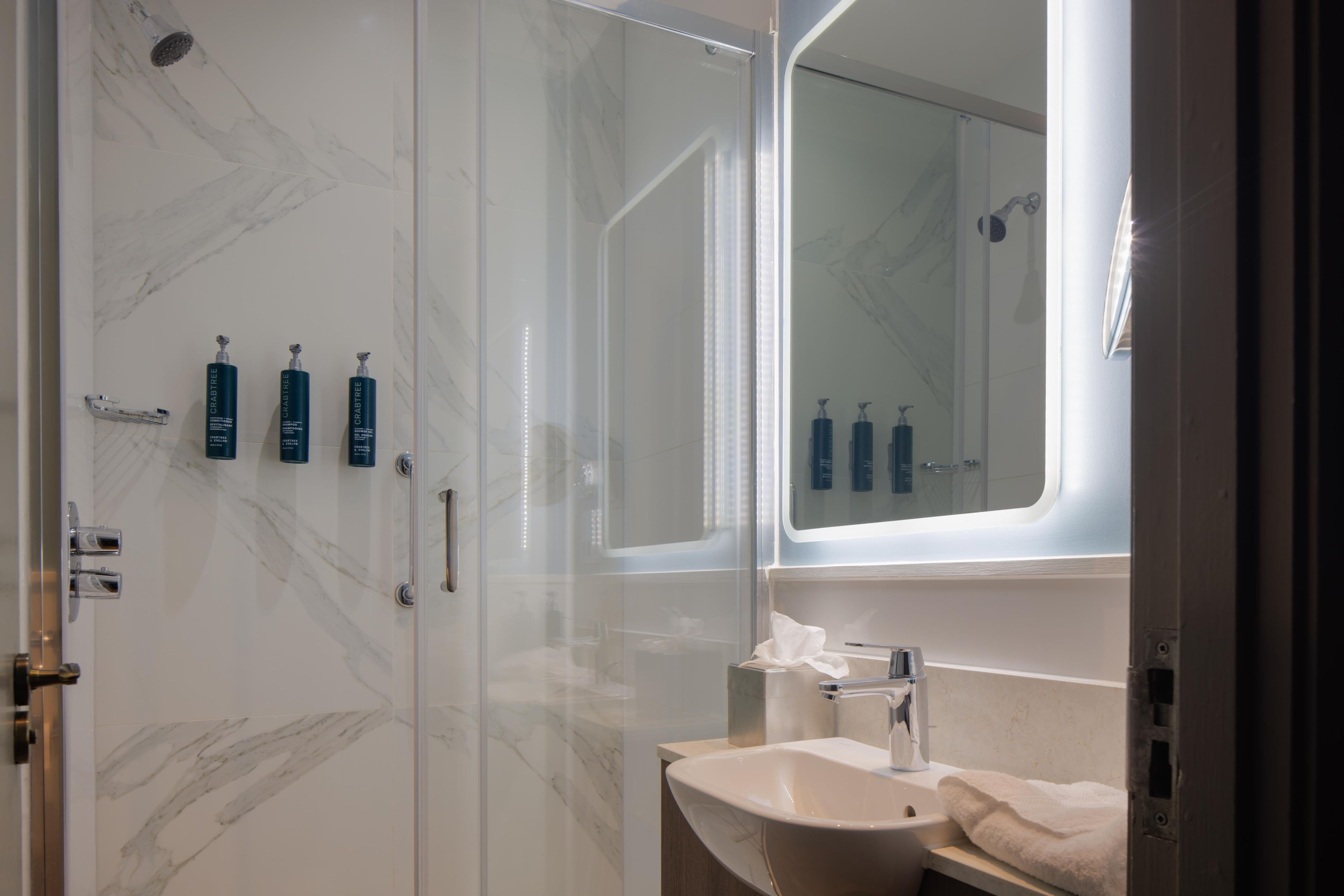 Ein Badezimmer mit Marmorwand, einem Waschbecken, einem Spiegel und drei Flaschen Crabtree Shampoo.