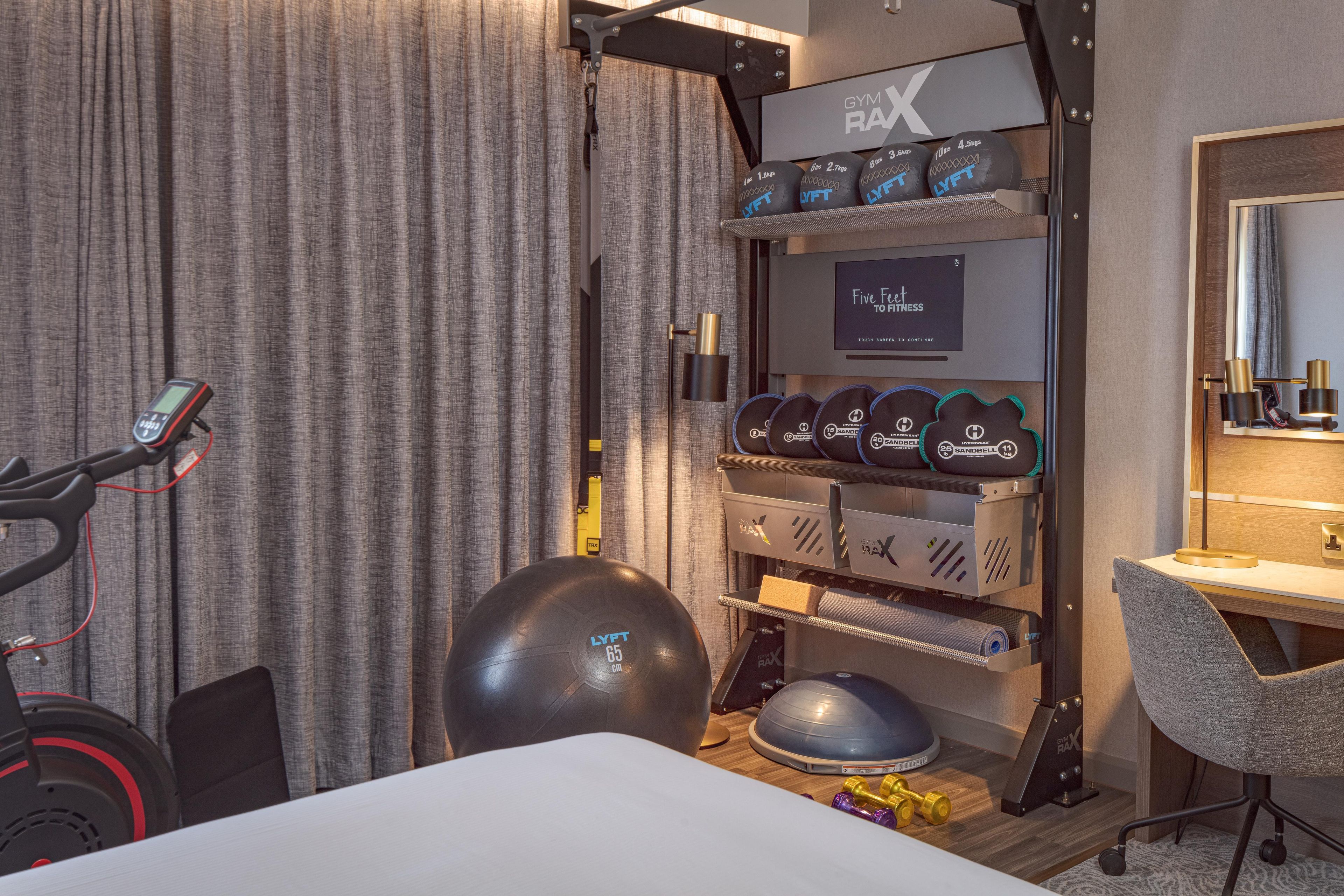 A hotel room with a workout area including a treadmill, exercise balls, and dumbbells.