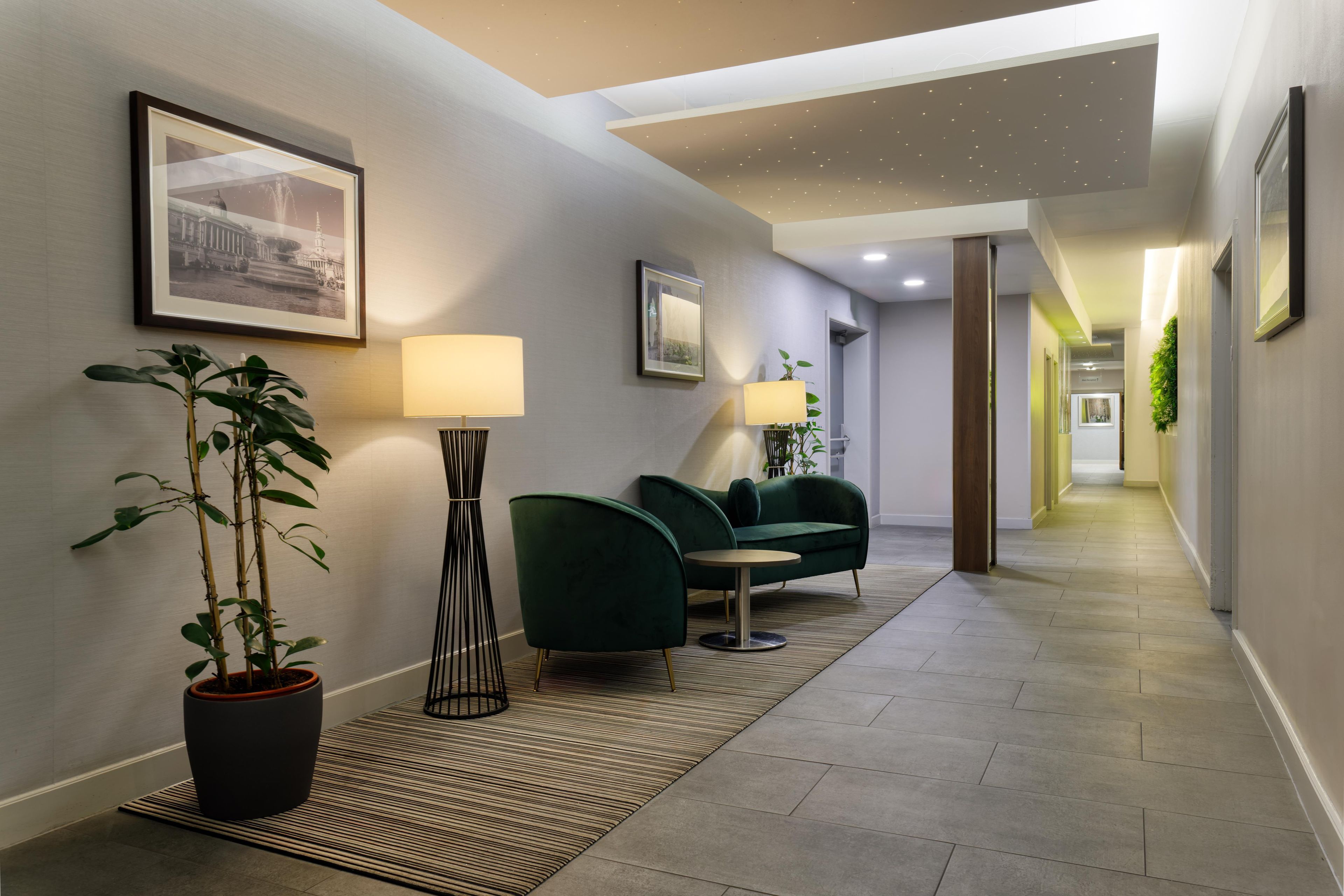 A hallway with a sofa, two lamps, a potted plant, and framed pictures on the walls.