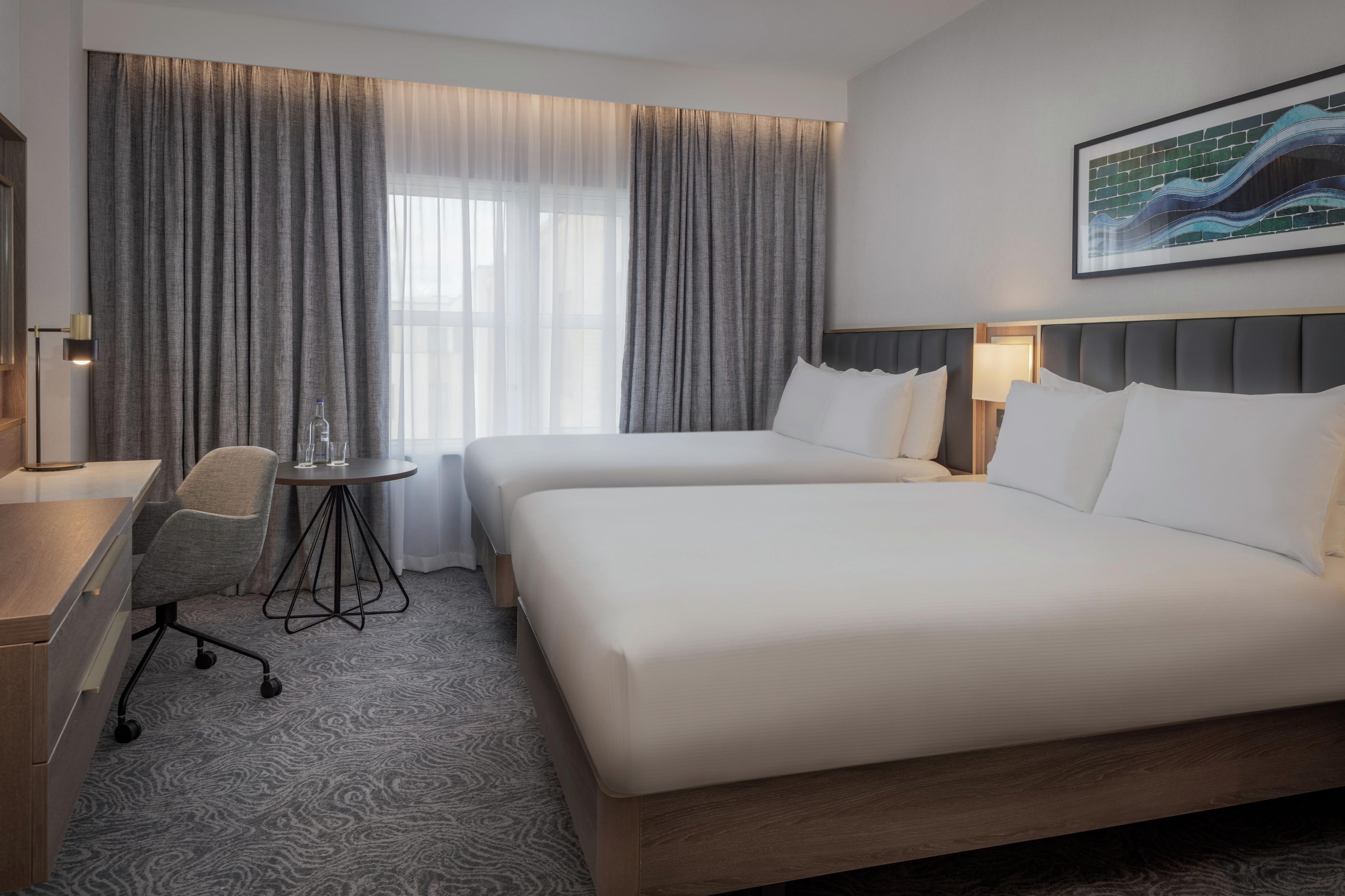 Una habitación de hotel con dos camas, un escritorio, una silla y una mesita.