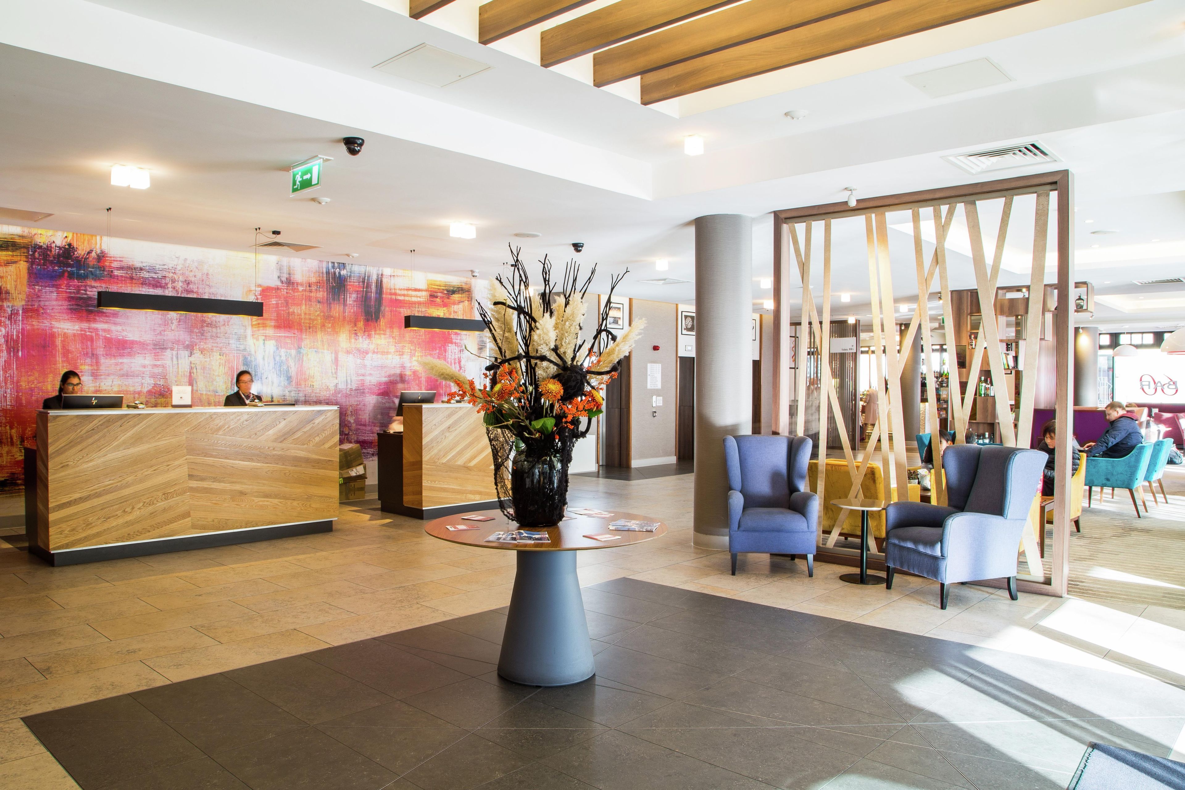 A reception area with a wooden reception desk, a vase with flowers, and blue chairs.