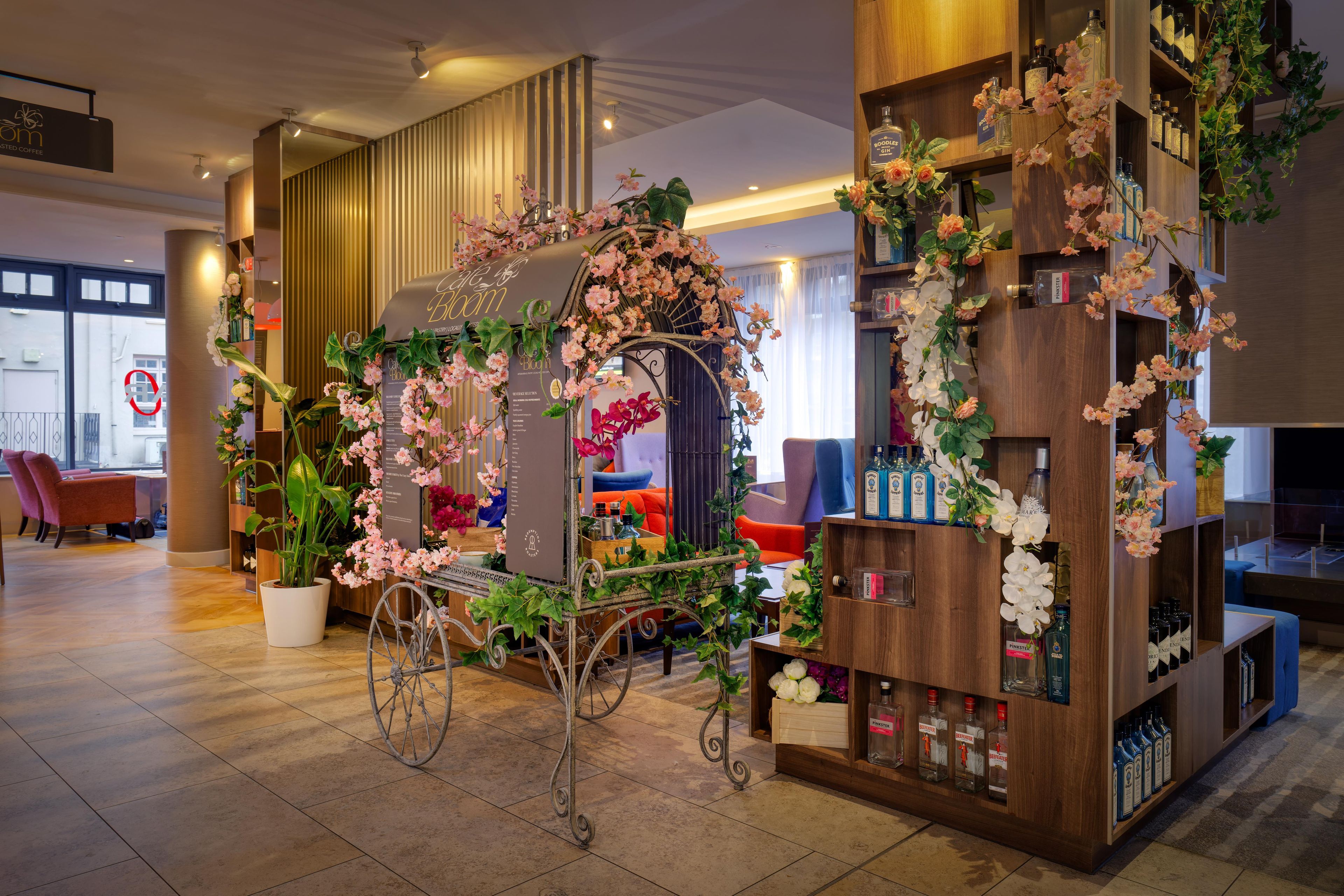 A cozy seating area with a decorative cart, a bookshelf with various bottles, and a sign indicating a coffee shop.