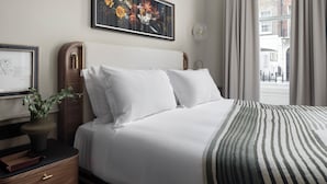 A neatly made bed with white linens, a striped throw blanket, and a wooden nightstand with drawers. - Montcalm Mayfair Townhouse (London)