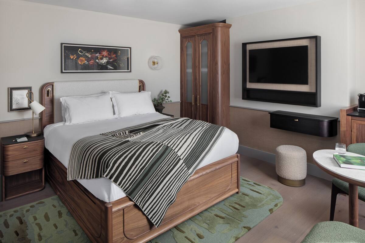 Un dormitorio ordenado con cama, mesita de noche, lámpara y televisor montado en la pared.