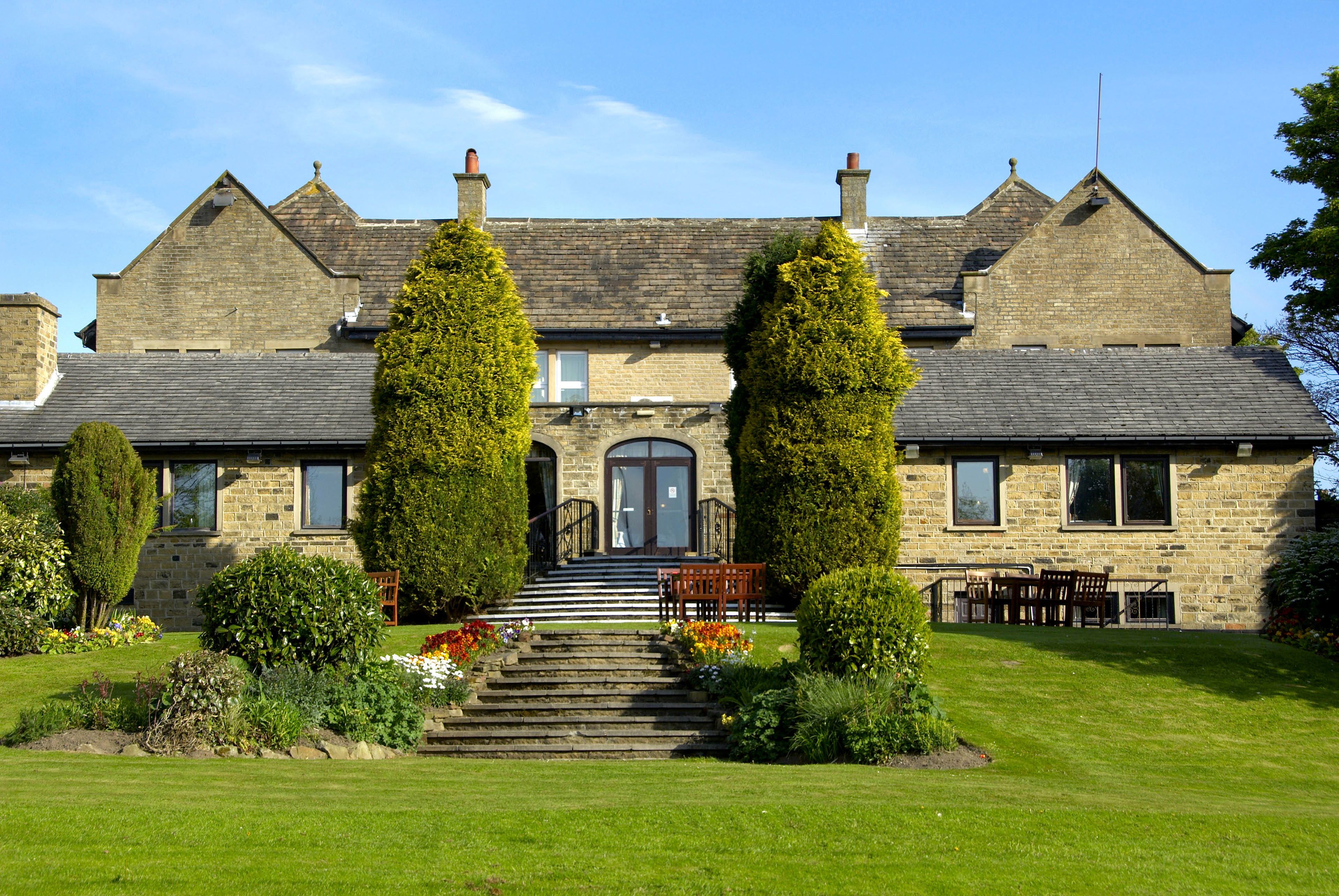 A stone building with a symmetrical facade, a central entrance with steps, and a well-maintained garden with various plants and flowers.