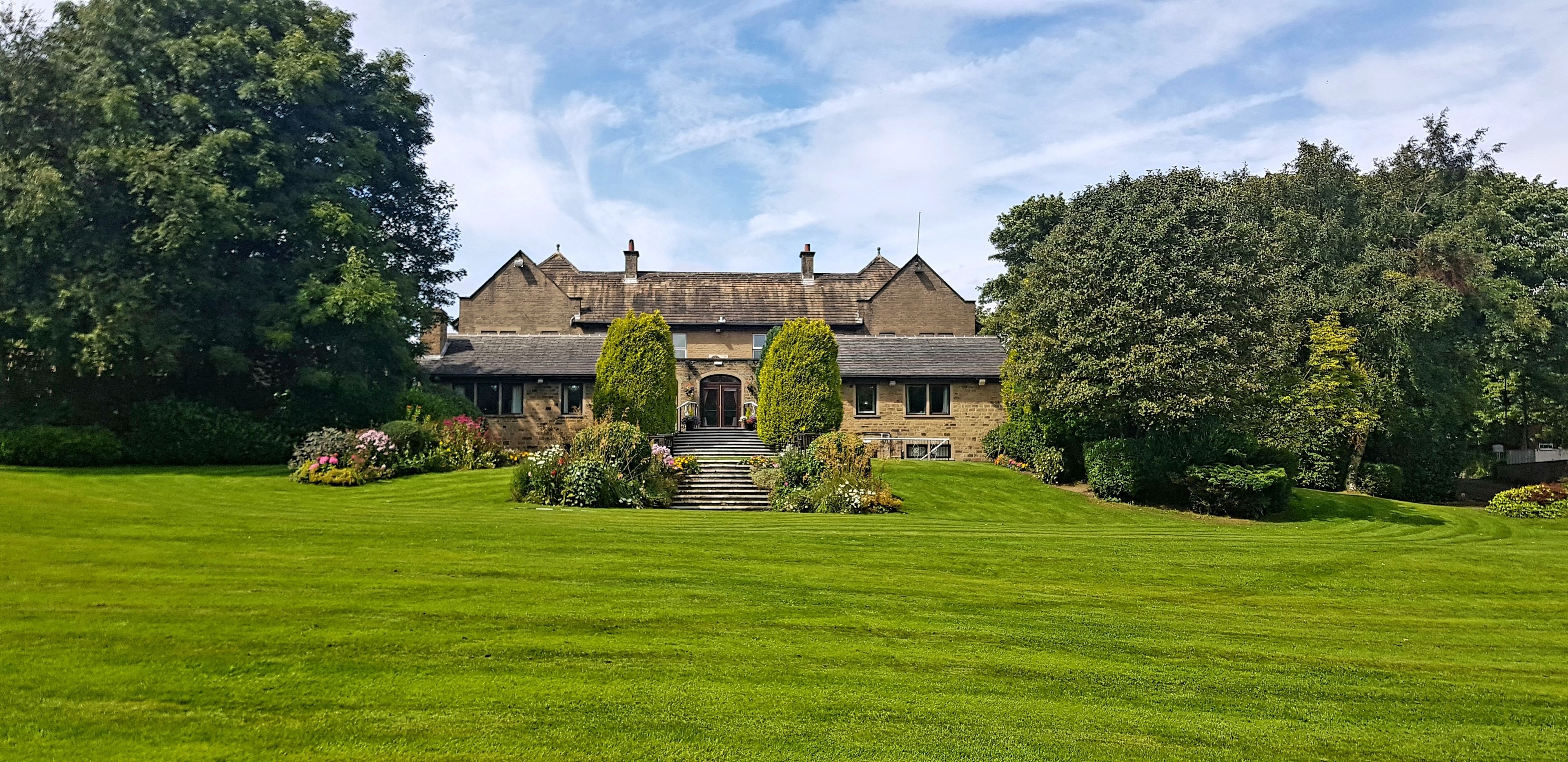 A large, traditional stone building with a symmetrical facade, surrounded by well-maintained lawns and mature trees.