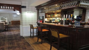 Una zona de bar con taburetes, una barra con grifos y estantes con botellas.
