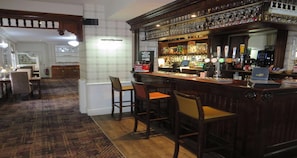 Una zona de bar con taburetes, una barra con grifos y estantes con botellas.