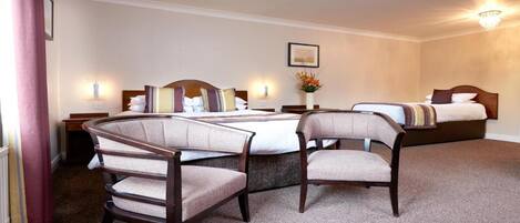 A hotel room with a large bed, two bedside tables, two chairs, a carpeted floor, and a chandelier.
