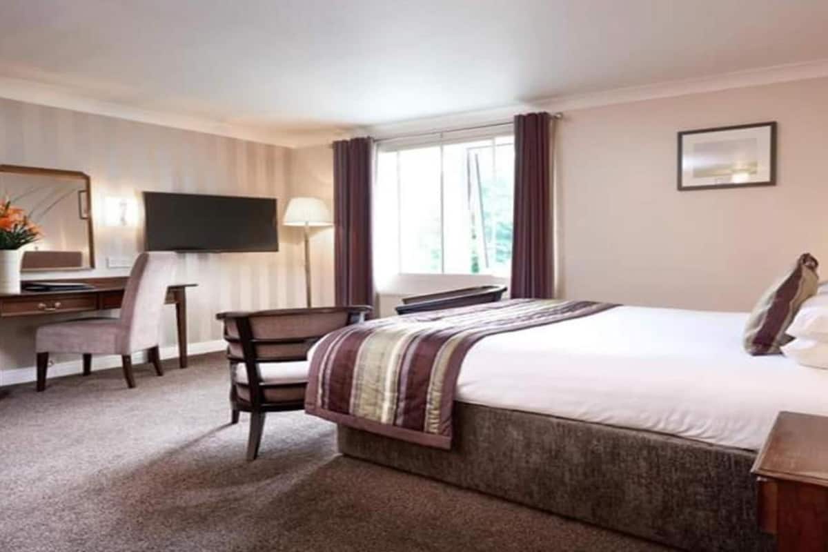 A hotel room with a bed, a desk, a chair, a television, and a window with curtains.