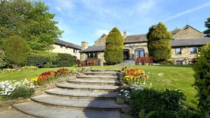 Una escalera de piedra conduce a un edificio con fachada de piedra tradicional y un jardín cuidado, con flores coloridas y setos podados.
